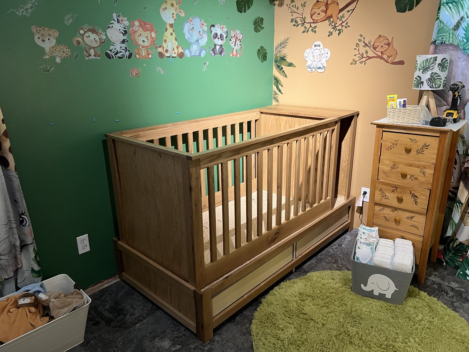 Wooden nursery crib with slatted sides, lower drawers, and a cabinet at one end